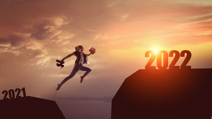 Silhouette woman jumping between cliff with number 2021 to 2022 and birds flying at tropical sunset beach.