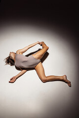 High angle view of young flexible, graceful girl, female contemp dancer in art performance isolated on dark studio background in spotlight.