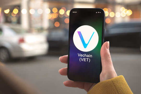 Vechain VET cryptocurrency symbol, logo. Business and financial concept. Hand with smartphone, screen with crypto icon close-up