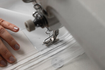 The seamstress deftly works on a sewing machine and sews white curtains. Close-up view.