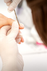 Close up of manicure master with manicure scissors removes cuticles on female nails at a beauty salon