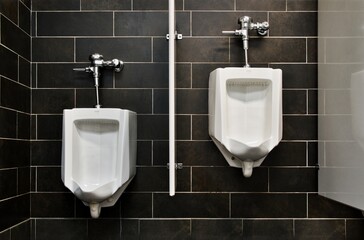 Two empty urinals in a public restroom with a black tile background wall.