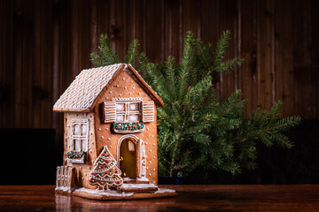 Homemade gingerbread house with glaze standing on table with  Christmas tree. Holiday mood,...
