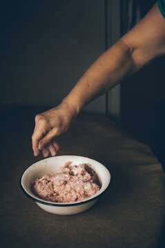 Elderly woman salts minced meat in bowl on kitchen table