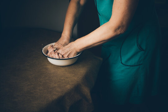 Elderly woman kneads minced meat in bowl on kitchen table