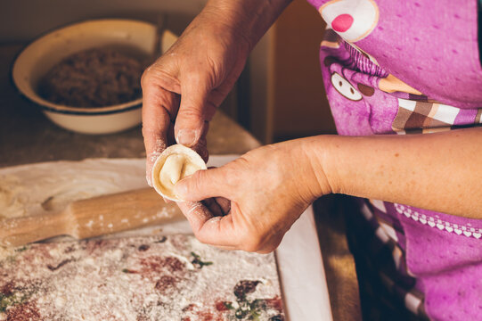 An elderly woman makes dumplings from dough with meat