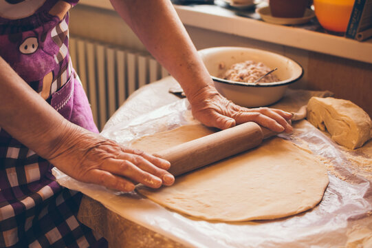 Woman in apron rolls out dough in flour on table