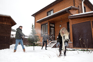 Man, young woman and adult woman playing snowballs near Christmas tree