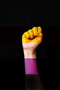Fist hand with non-binary pride flag patterned isolate on black.
