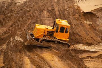 large yellow caterpillar industrial tractor, iron dump shifts sand and ground, lines road for transport inside development of large sandy career.