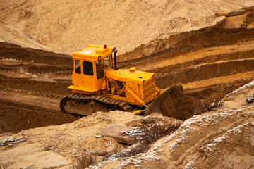 Obraz premium large yellow caterpillar industrial tractor, iron dump shifts sand and ground, lines road for transport inside development of large sandy career.