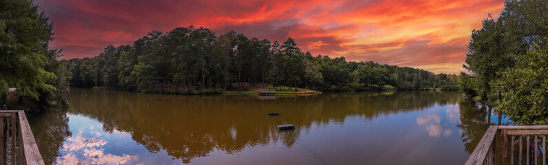 Fototapeta na wymiar a stunning aerial panoramic shot of the still green lake surrounded by lush green and autumn colored trees with powerful clouds at sunset at Duncan Park in Fairburn Georgia USA