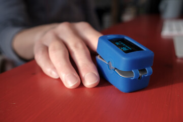 Woman uses a pulse oximeter to measure pulse rate and blood oxygen levels on a red table in an...