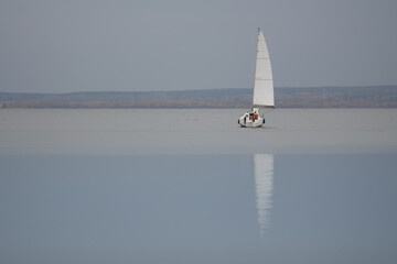 Horizontal monochromatic seascape view of a single white sailing boat on a smooth blue water...