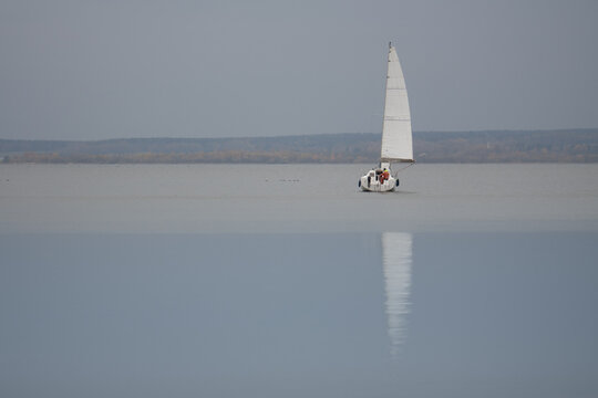 Horizontal Monochromatic Seascape View Of A Single White Sailing Boat On A Smooth Blue Water Surface At Calm Autumn Misty Day