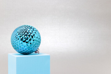 Blue Christmas bauble on a podium in front of silver colored background.