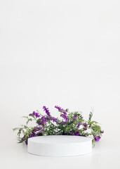 White podium on the white background with flowers. Podium for product, cosmetic presentation. Creative mock up. Pedestal or platform for beauty products.