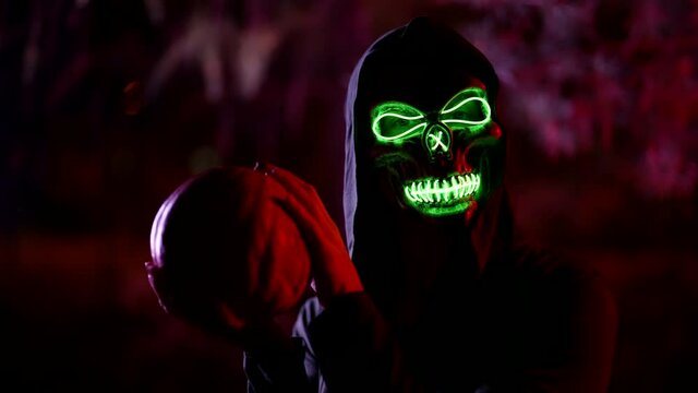 enigmatic deathless character with glowing skull is playing with pumpkin in Halloween night