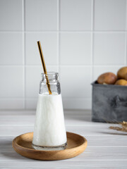 Dairy-free potato milk for vegans in glass bottle with metal straw on wooden plate. Alternative plant-based drink and potatoes in metal box on kitchen table. Selective soft focus.