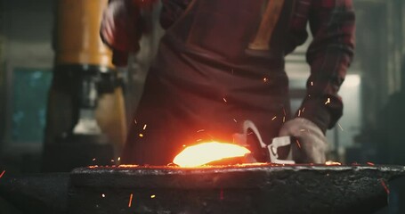 Close-up of blows on hot metal, sparks flying in different directions. The blacksmith holds the workpiece with one hand with tongs, and with the other a hammer with which he forges the product - Powered by Adobe