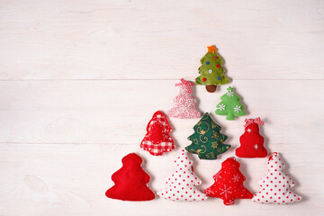New Year card with colored soft toy trees laid out in the shape of a Christmas tree on a white wooden background. Flat