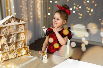 A smiling  pretty girl with sweets in hand, finding gift in toys wooden house of Christmas Advent...