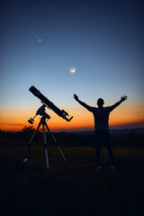 Silhouette of a man, telescope and countryside under the starry skies.