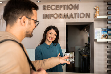 Smiling female receptionist behind the hotel counter showing guest available rooms on tablet.