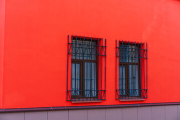 Red facade of the building with wooden windows on which there are iron bars for protection.