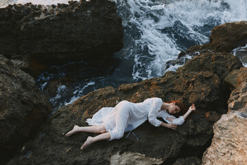 beautiful young woman lying on rocky coast with cracks on rocky surface landscape