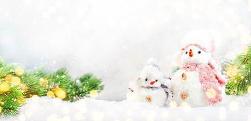 Christmas snow composition with two cute snowmen in hats and scarves in snowdrift and fir branches on gray background