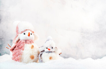 Christmas and new year snow concept with two cute snowmen in hats and scarves in snowdrift on gray background