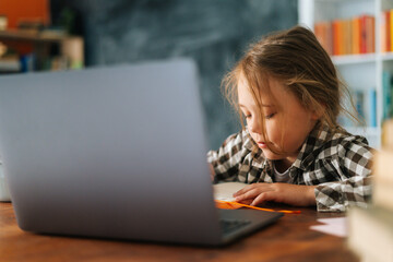 Close-up of focused primary child school girl doing homework writing notes in paper notebook...
