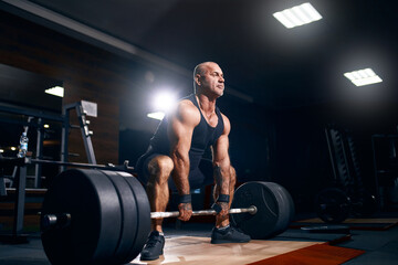Adult bald powerlifter bodybuilder exercising deadlift barbell in gym. Powerlifting. Bodybuilding