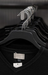 A selection of generic black V-neck shirts hanging on a clothes rail by coat hangers. The identical...