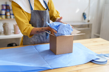 E-commerce and shipment: cropped image of female craft ceramist packing handmade potter for...