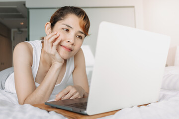 Asian woman works with laptop on the bed. Concept of work from hotel.
