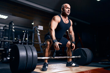 Fototapeta na wymiar Adult bald male powerlifter bodybuilder preparing deadlift barbell in gym. Powerlifting Bodybuilding
