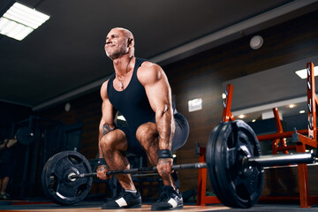Fototapeta na wymiar Bodybuilder muscular man doing heavy deadlift exercise with weight while in gym over dark background