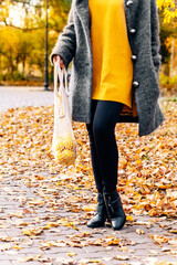 ECO bag with lemons is carried by a woman in an autumn park in a yellow sweater and coat. Waste-free use the concept of careful ecology. Fruits and vegetables in a grid in nature, outdoors