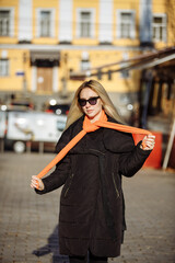Fototapeta premium girl in black clothes with an orange scarf wearing glasses on the background of the city