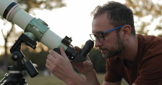 Man looking through a astronomical telescope outdoors.	
