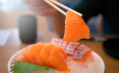 Using chopsticks, salmon sashimi. Sashimi is a popular dish of Japanese restaurants.