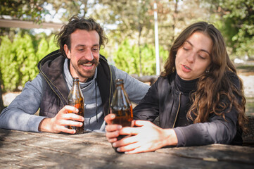 Smiling cheerful young couple, boyfriend and girlfriend, drinks bottle beer