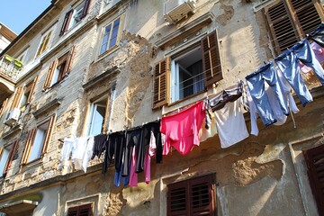 old, crumbling wall, open window in an old building, laundry hanging on a string, falling plaster, old building, poor district, dilapidated walls, colorful laundry, old shutters