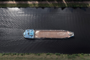 Aerial top-down view of a self-propelled barge without cargo going along a narrow channel