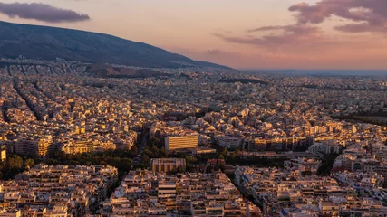 Poster Panoramisch stadsbeeld van Athene, Griekenland bij zonsondergang met gebouwen fel verlicht door de zon © Igor