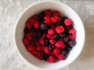 Red and black berries in a white bowl on a tablecloth