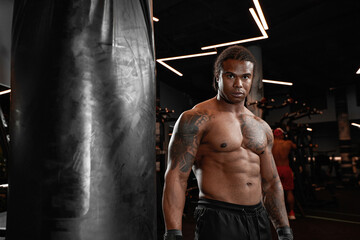 Fototapeta na wymiar An African American guy trains in gym and fists his boxing bag fists. Concept of: gym, fitness, boxing, success, workout and power