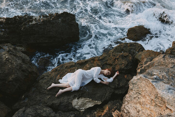 Beautiful bride in a secluded spot on a wild rocky coast in a white dress landscape
